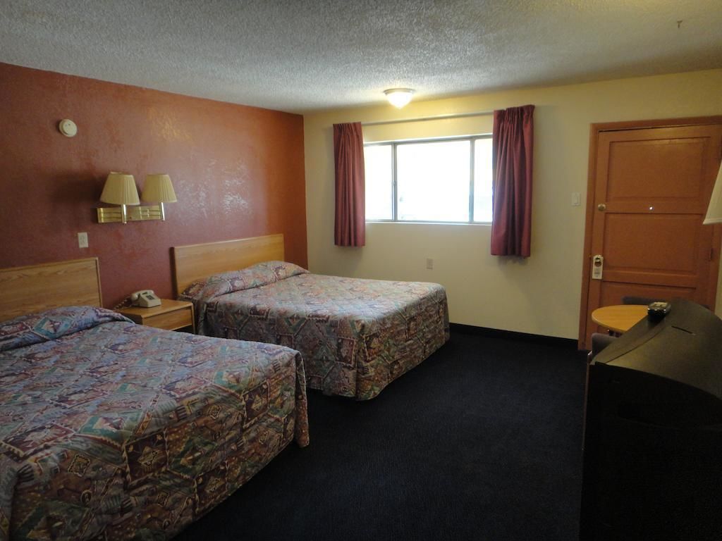 A hotel room with two beds, a desk, a chair, a window with curtains, and a door.