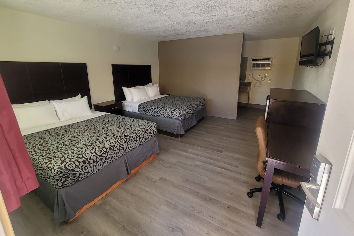 Une chambre d’hôtel avec deux lits, un bureau, une chaise, une télévision et un appareil de climatisation.