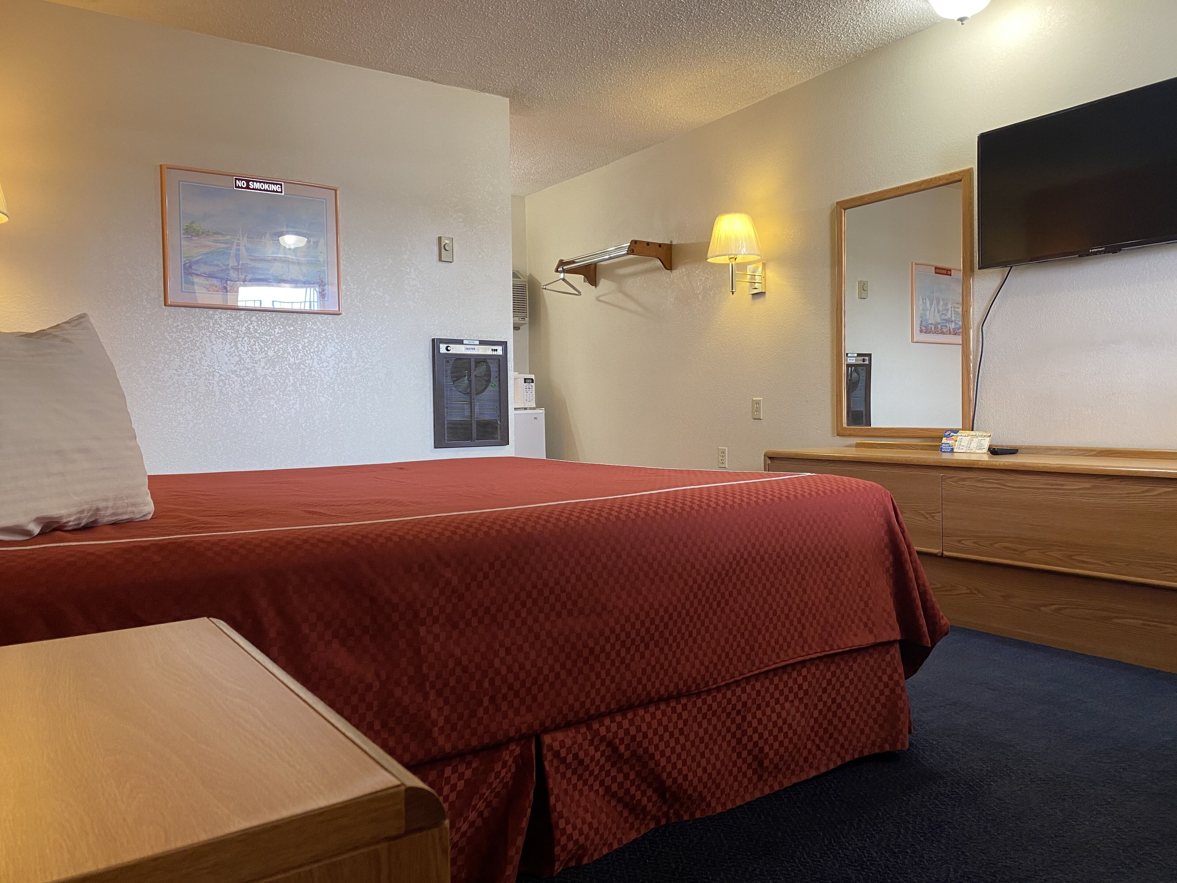 Habitación de hotel con cama, escritorio, cómoda, espejo, televisor y un calentador instalado en la pared.
