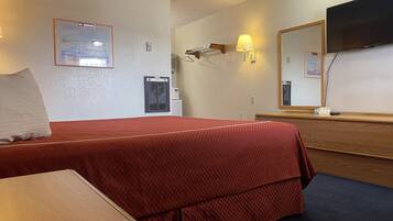 Habitación de hotel con cama, escritorio, cómoda, espejo, televisor y un calentador instalado en la pared.