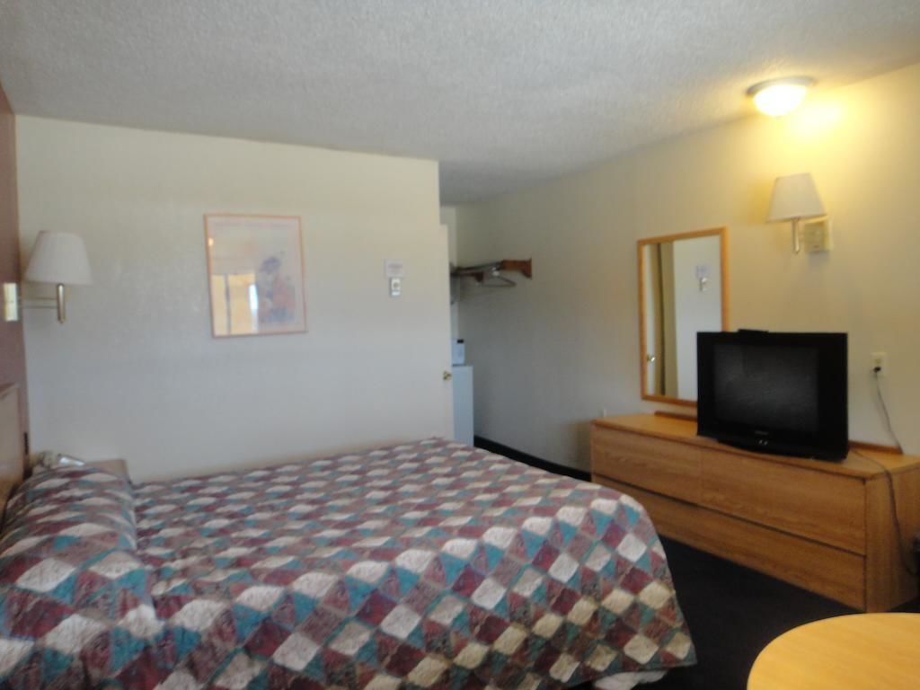 A hotel room with a bed, a dresser with a television, a mirror, and a lamp.