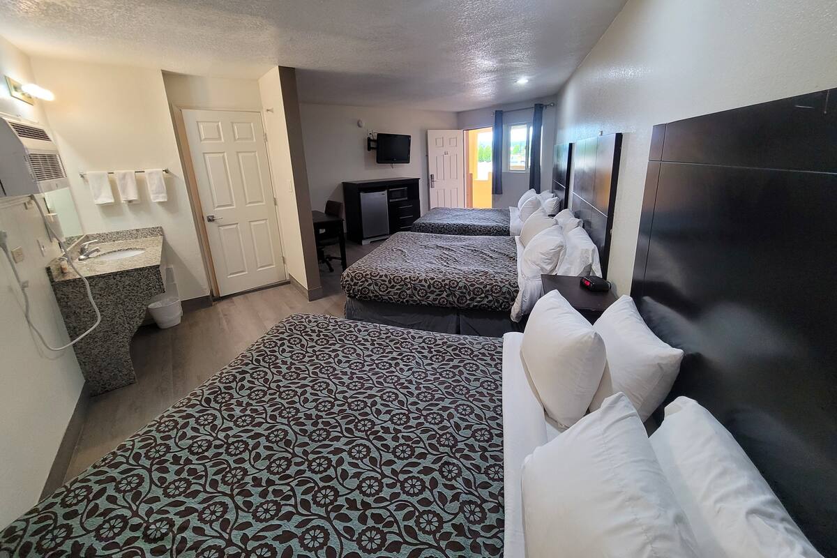 Une chambre d’hôtel avec deux lits, un bureau, une télévision et une salle de bain équipée d’un lavabo et d’un porte-serviettes.