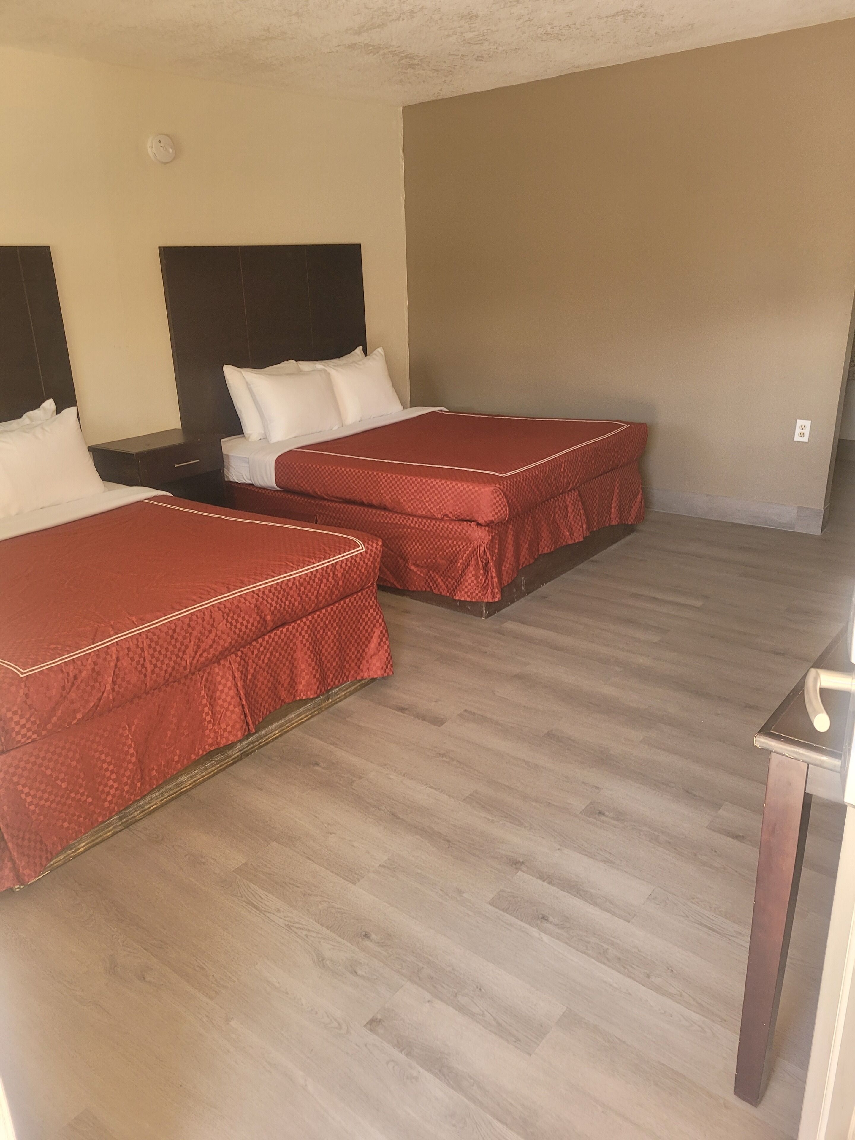 Une chambre d’hôtel avec deux lits, un plancher en bois et un mur uni.