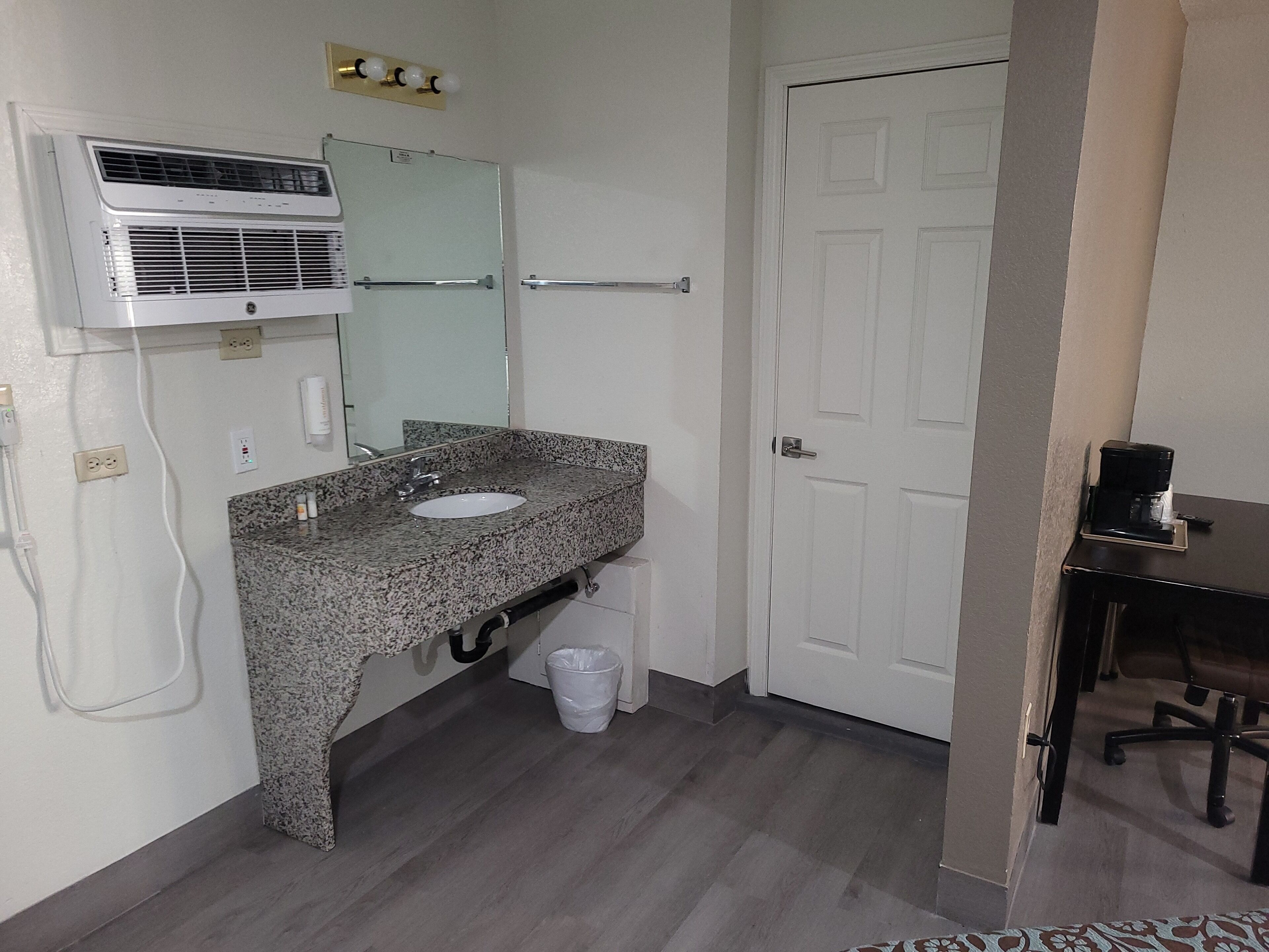 A bathroom with a granite countertop sink, a mirror, a white door, and a coffee maker on a table.