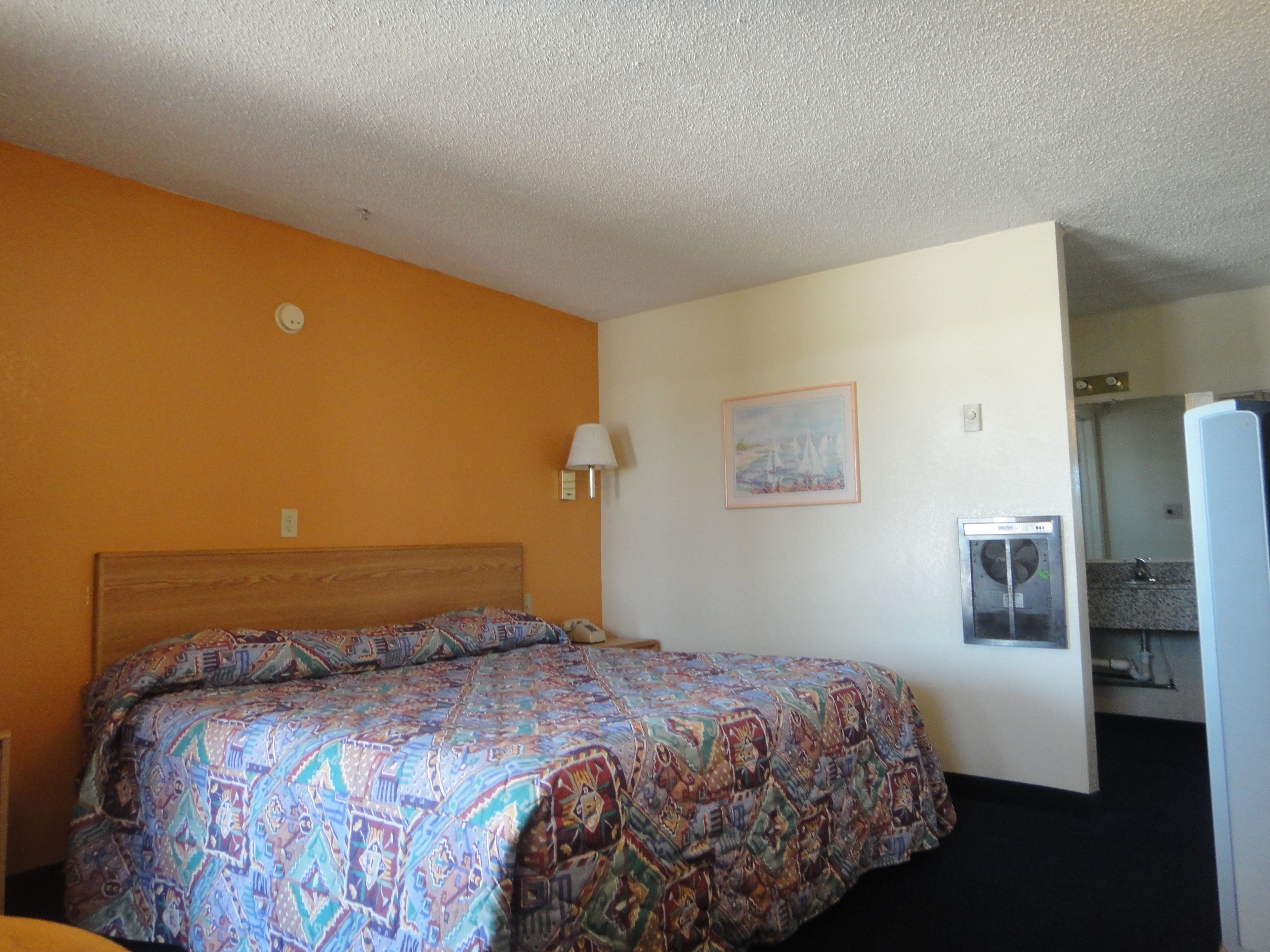 A hotel room with a bed, a painting on the wall, and a bathroom visible through an open door.