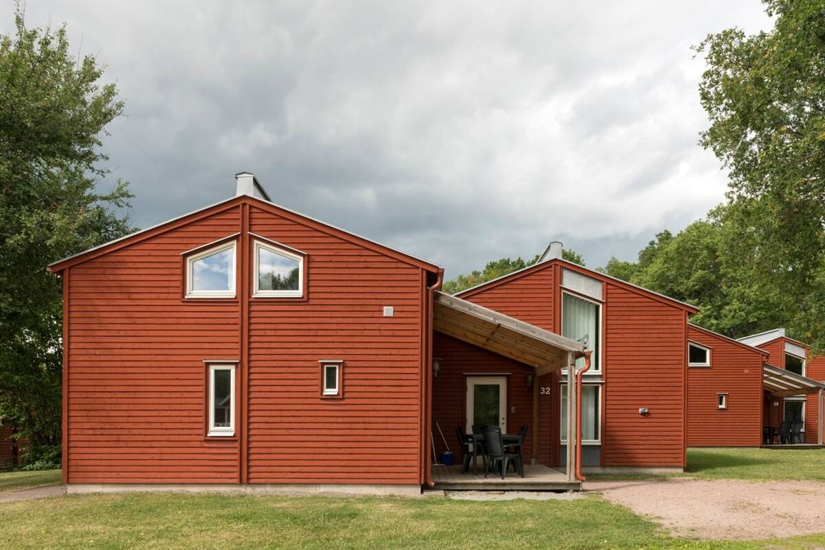 A red wooden building with a covered porch and a door, number 32, in a grassy area with trees in the background.