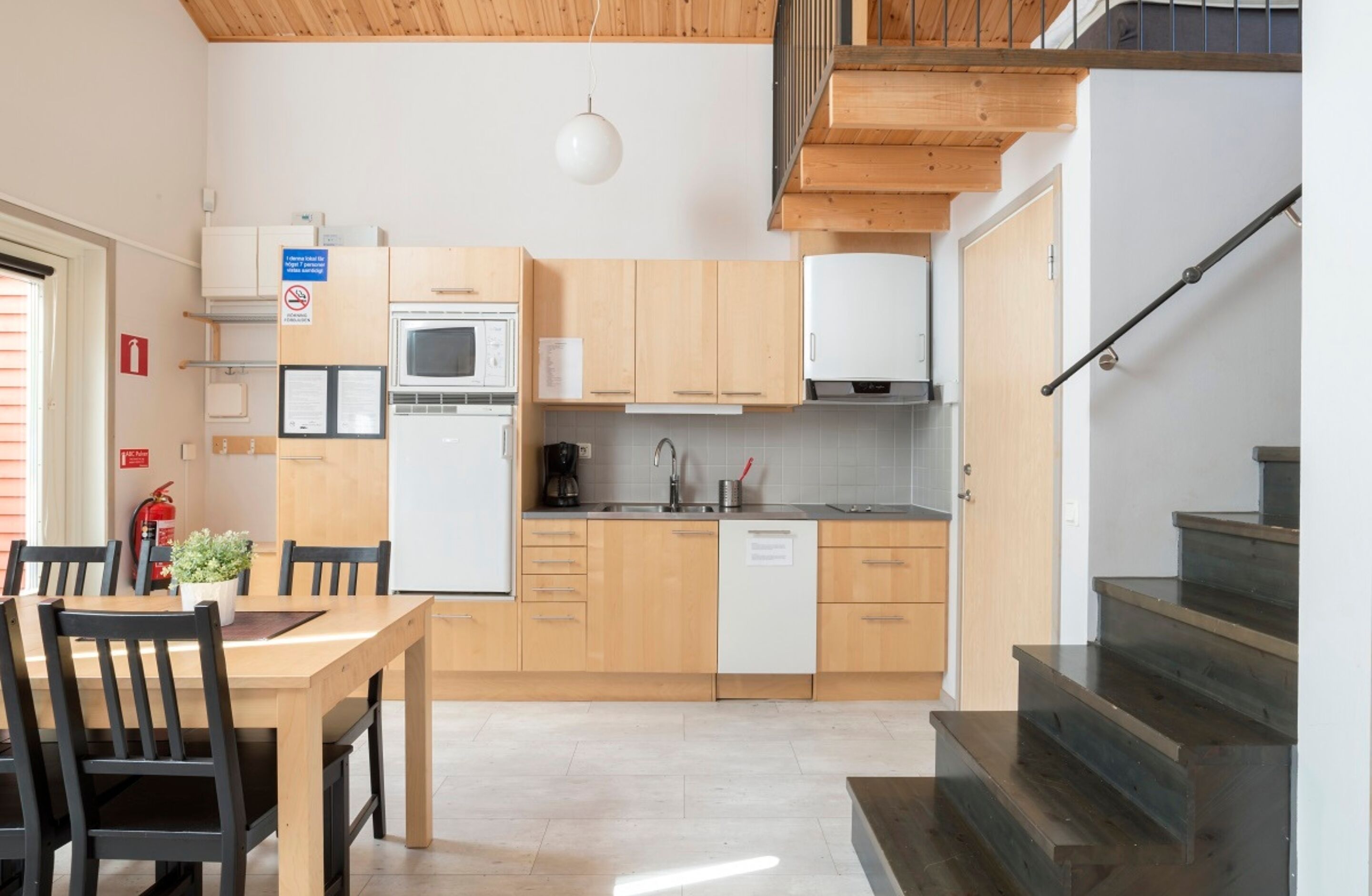 A compact kitchen with wooden cabinets, a white dishwasher, and a dining area with a table and chairs.