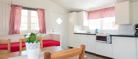 Une pièce comprenant une table à manger en bois, un canapé rouge, un meuble blanc et une fenêtre ornée de rideaux à carreaux.