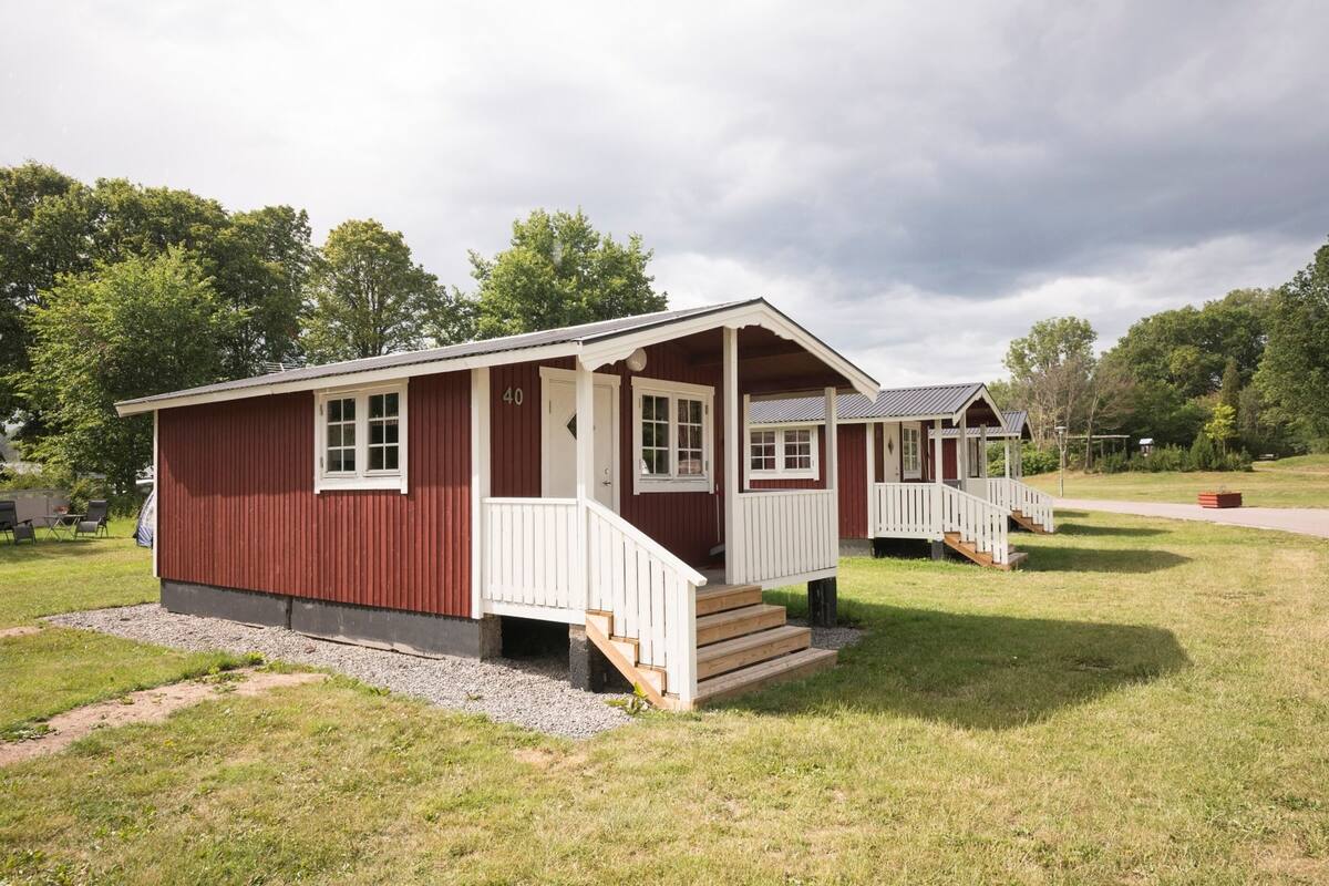 A red and white cabin-style building with a porch and steps, surrounded by grass and trees.