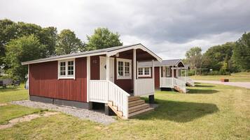A red and white cabin-style building with a porch and steps, surrounded by grass and trees.