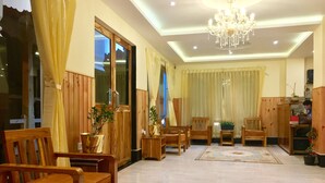 Un salón amplio con muebles de madera, una araña y un ventanal con cortinas.
