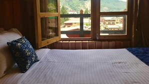 Una habitación con cama, ventana y vista a un paisaje montañoso, además de barandal de madera.