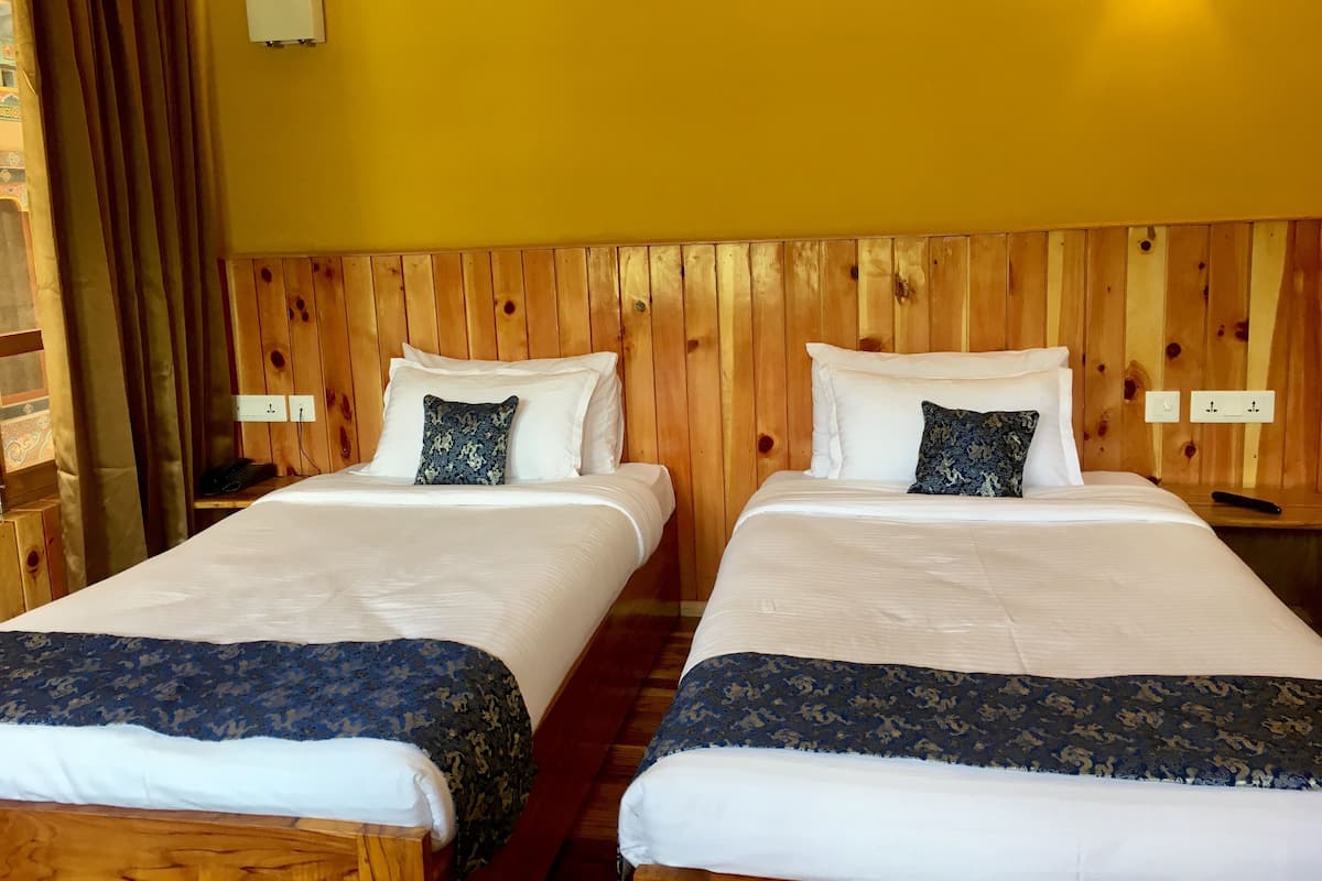 Dos camas individuales con cabeceros de madera, ropa de cama blanca y almohadones azul oscuro.