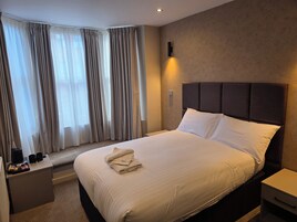 A hotel room with a large bed, a bedside table, a nightstand, and a window with curtains.