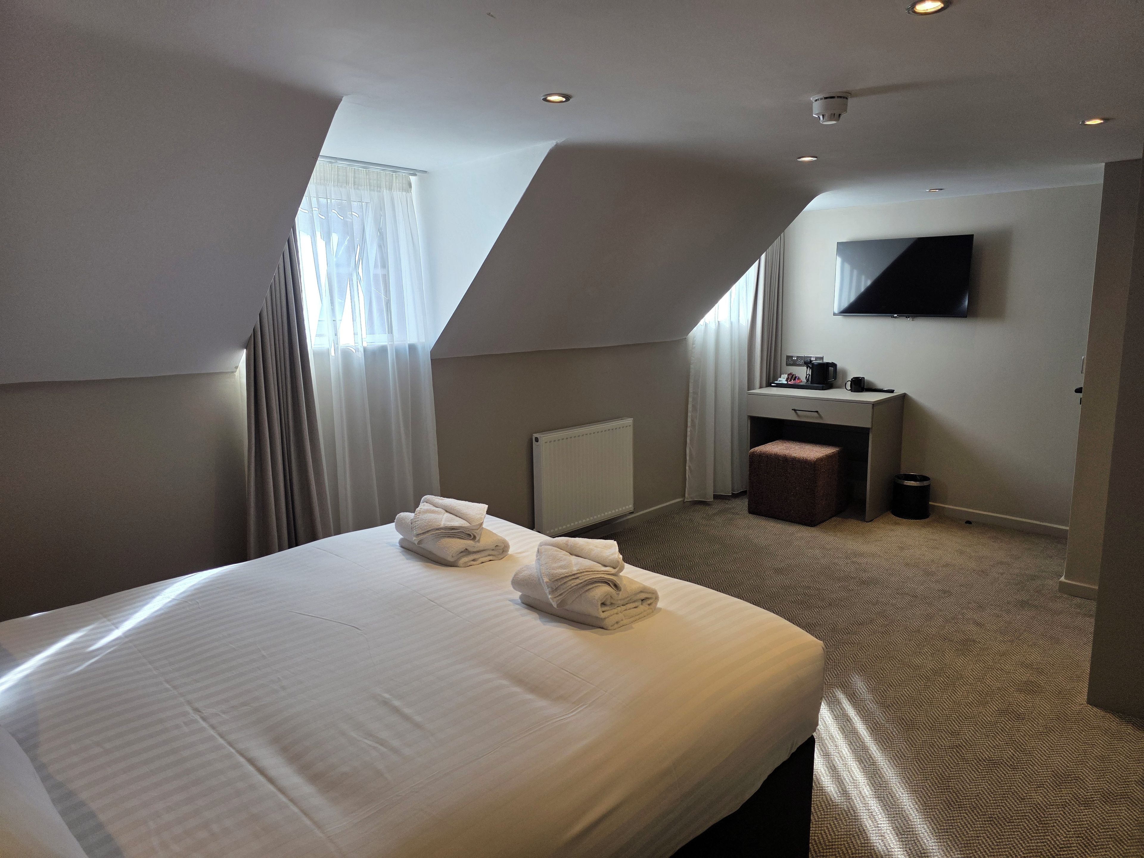 Ein Hotelzimmer mit einem großen Bett, einem Schreibtisch, einem Sessel, einem Flachbildfernseher und einem fenster mit Vorhängen.