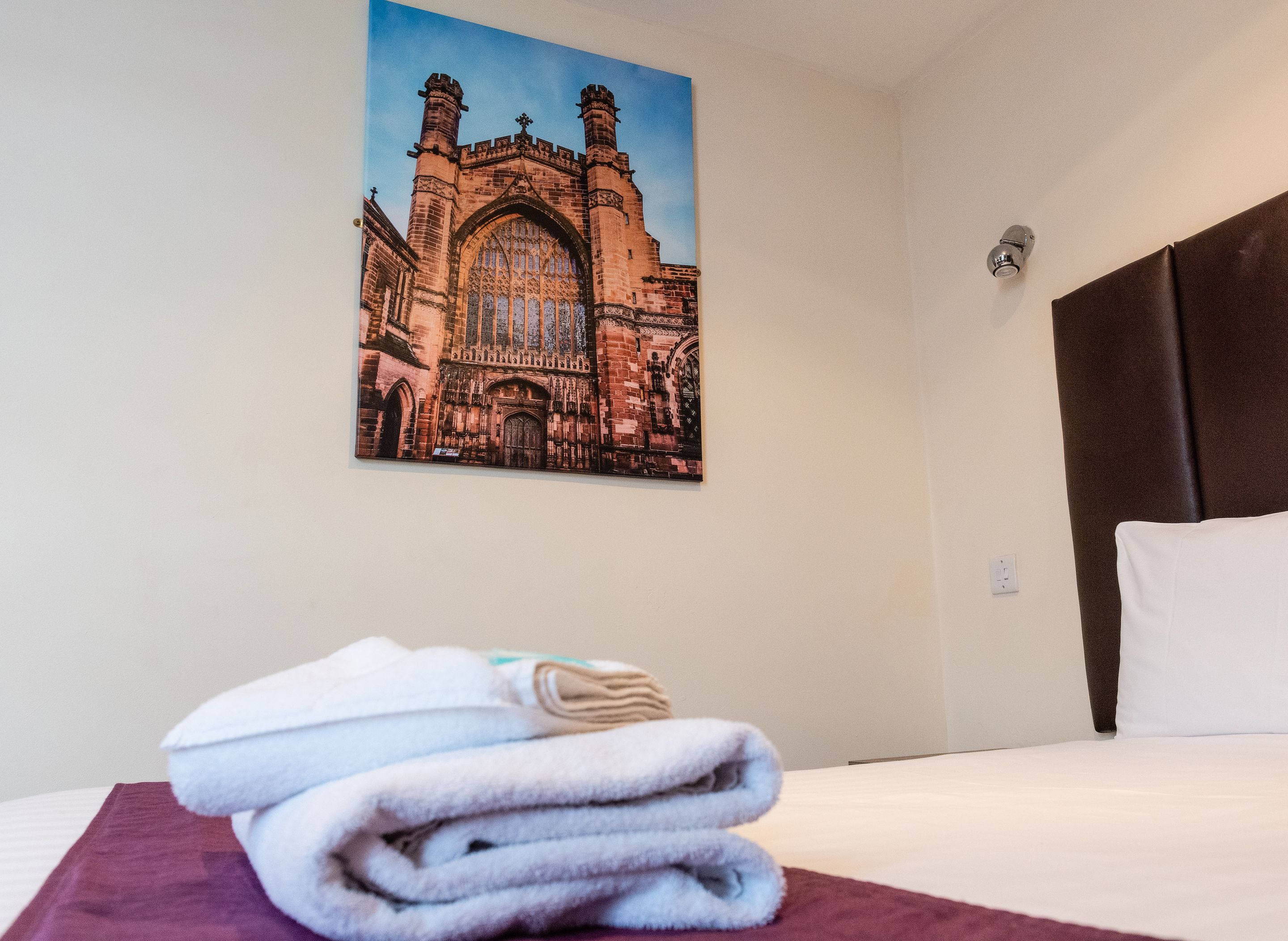 A hotel room with a bed, a folded towel, a framed picture of a building, and a headboard.