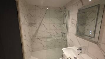 A modern bathroom with a glass-enclosed shower, a white sink, and a marble-tiled wall.