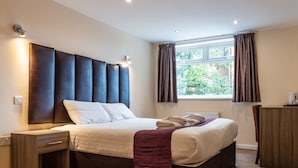 A modern bedroom with a large bed, bedside tables, a dresser, and a window with curtains. - Quarterz (Chester)