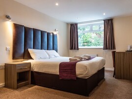 A modern bedroom with a large bed, bedside tables, a dresser, and a window with curtains.