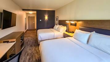 A hotel room with two beds, a desk, a chair, and a nightstand with a lamp.