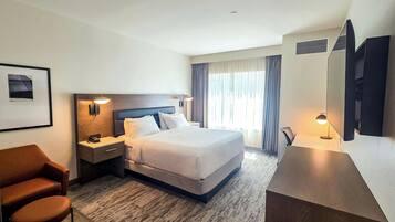 A hotel room with a bed, a desk, a chair, a TV, and a framed picture on the wall.