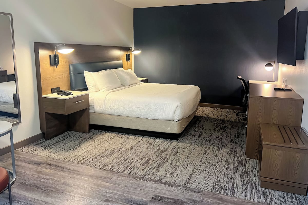 Quarto de hotel com cama, mesas de cabeceira, escrivaninha e uma cadeira.