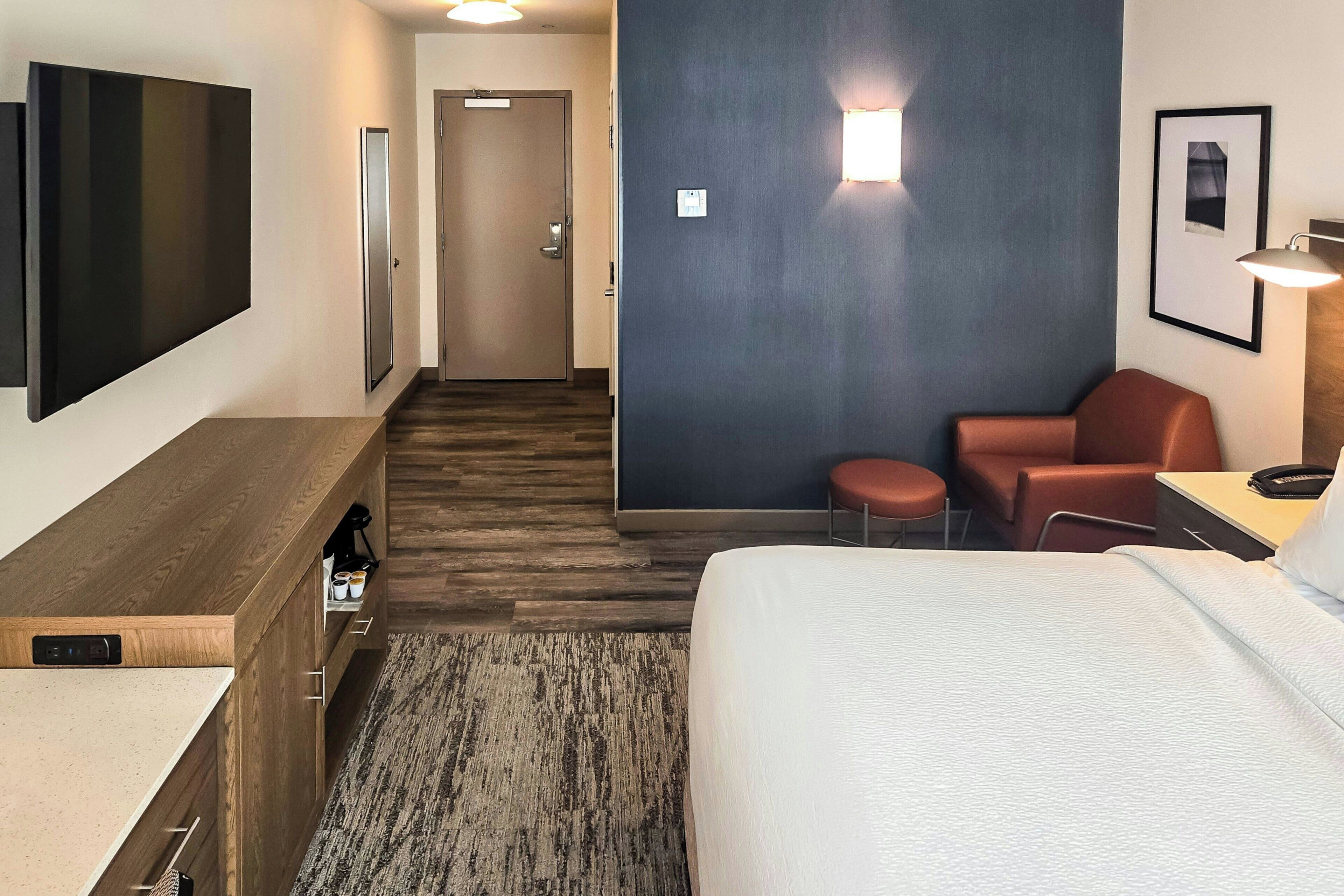 A hotel room with a bed, a desk, a chair, a TV, and a door.