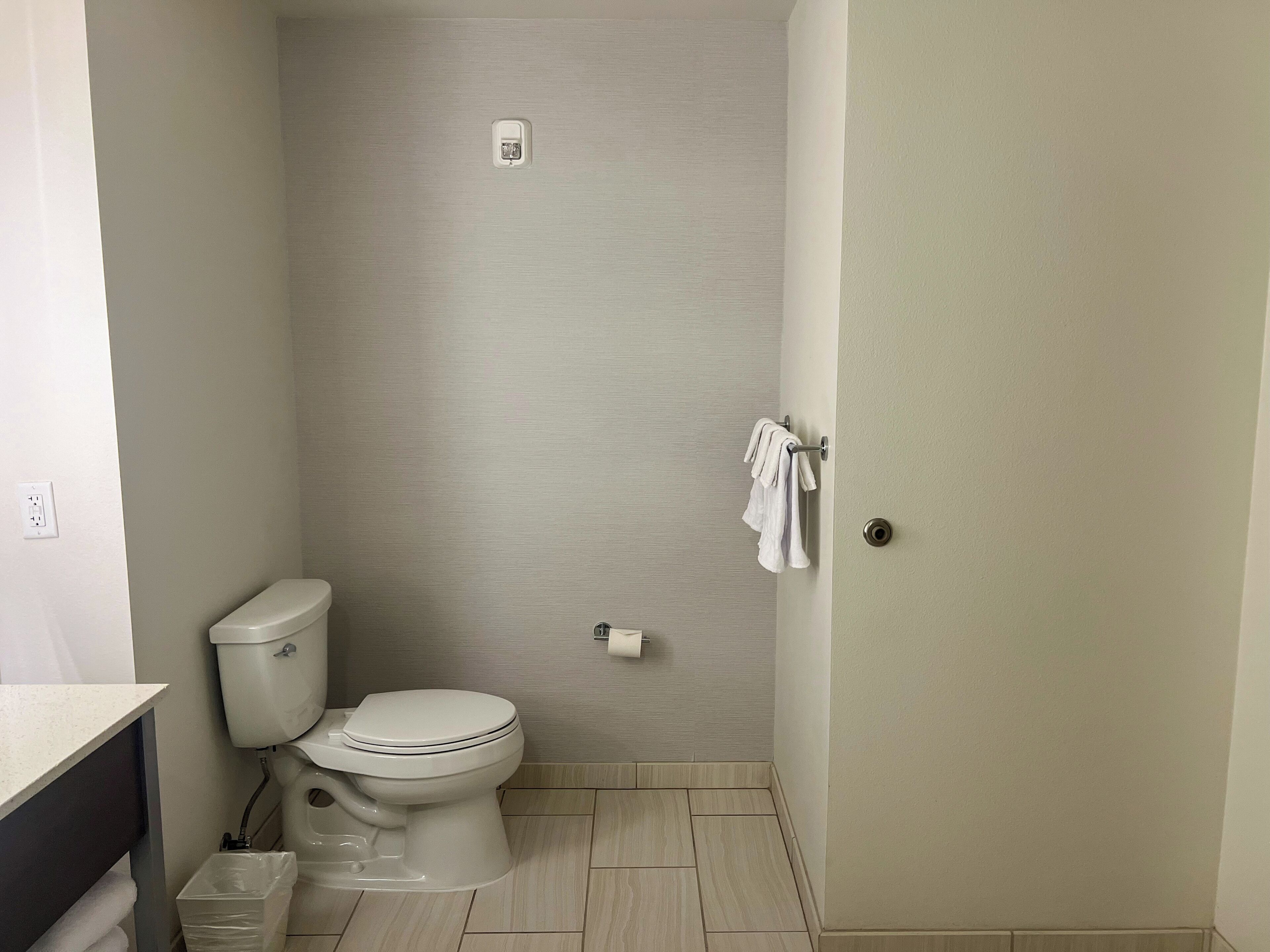 Un baño pequeño y limpio con inodoro, perchero y cubo de basura.