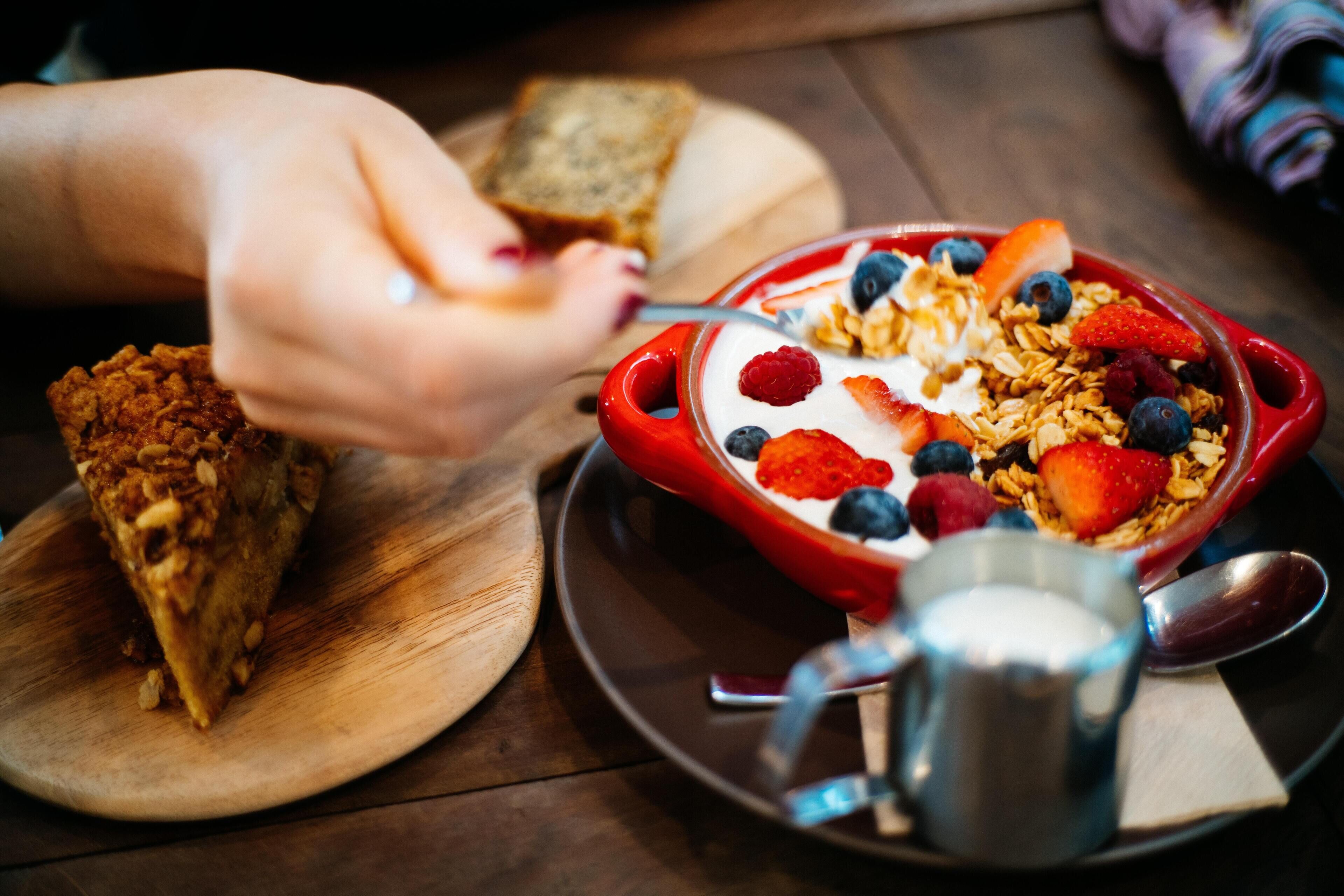 Un bol de céréales avec des fruits et du granola, une tranche de pain grillé et une carafe de lait sur une table en bois.