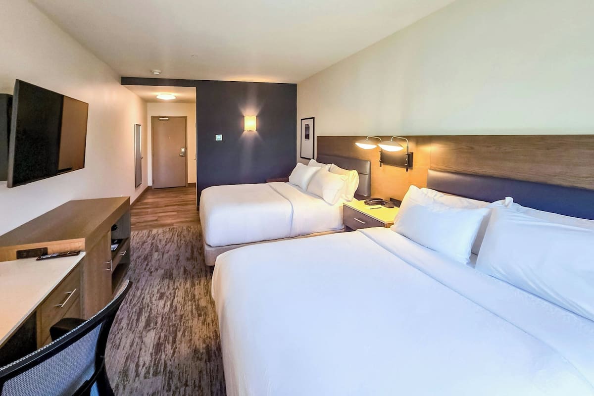 Quarto de hotel com duas camas, uma escrivaninha, uma cadeira, uma televisão e uma porta.