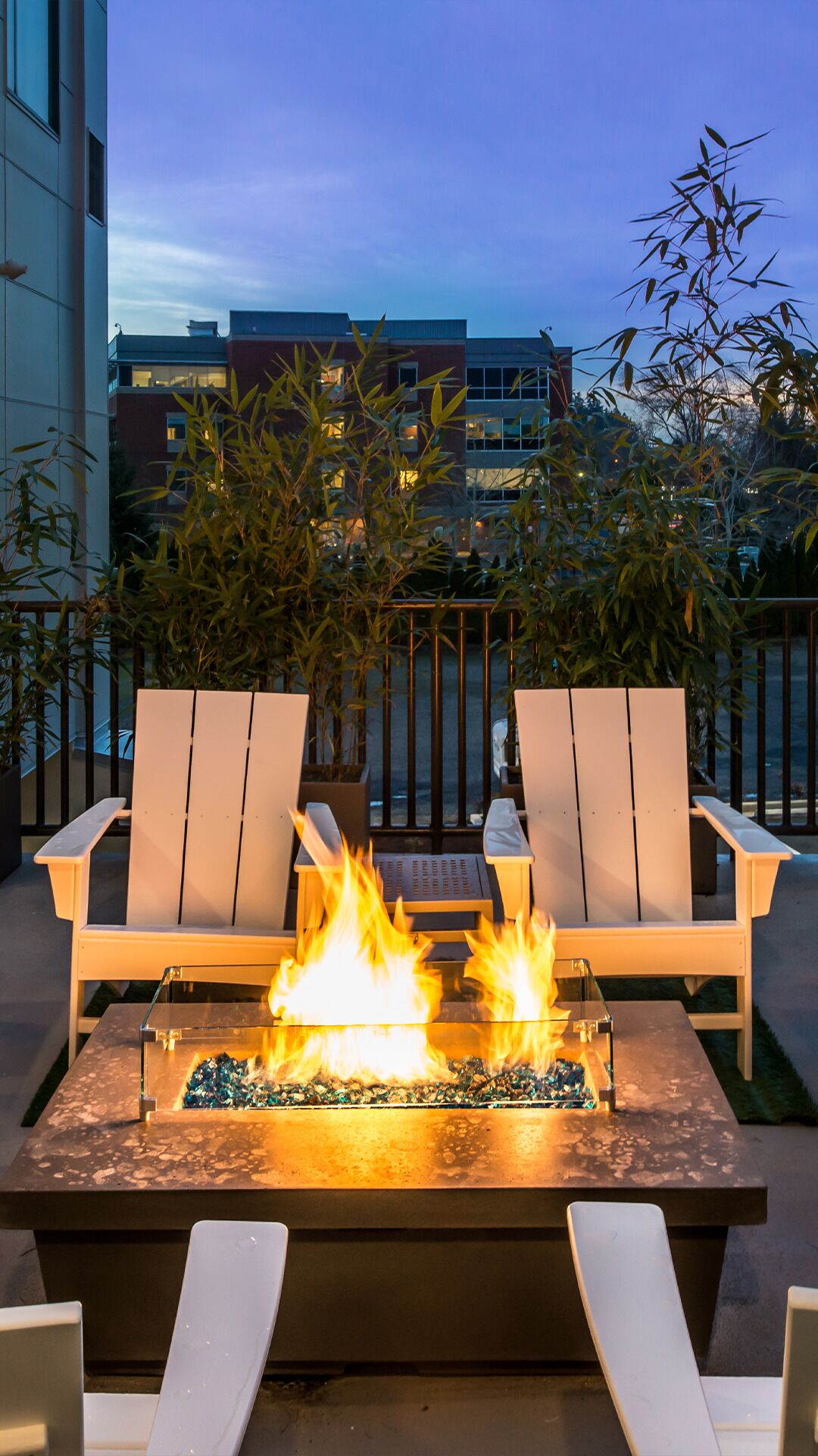 An outdoor seating area with a fire feature, surrounded by potted plants and overlooking a building.