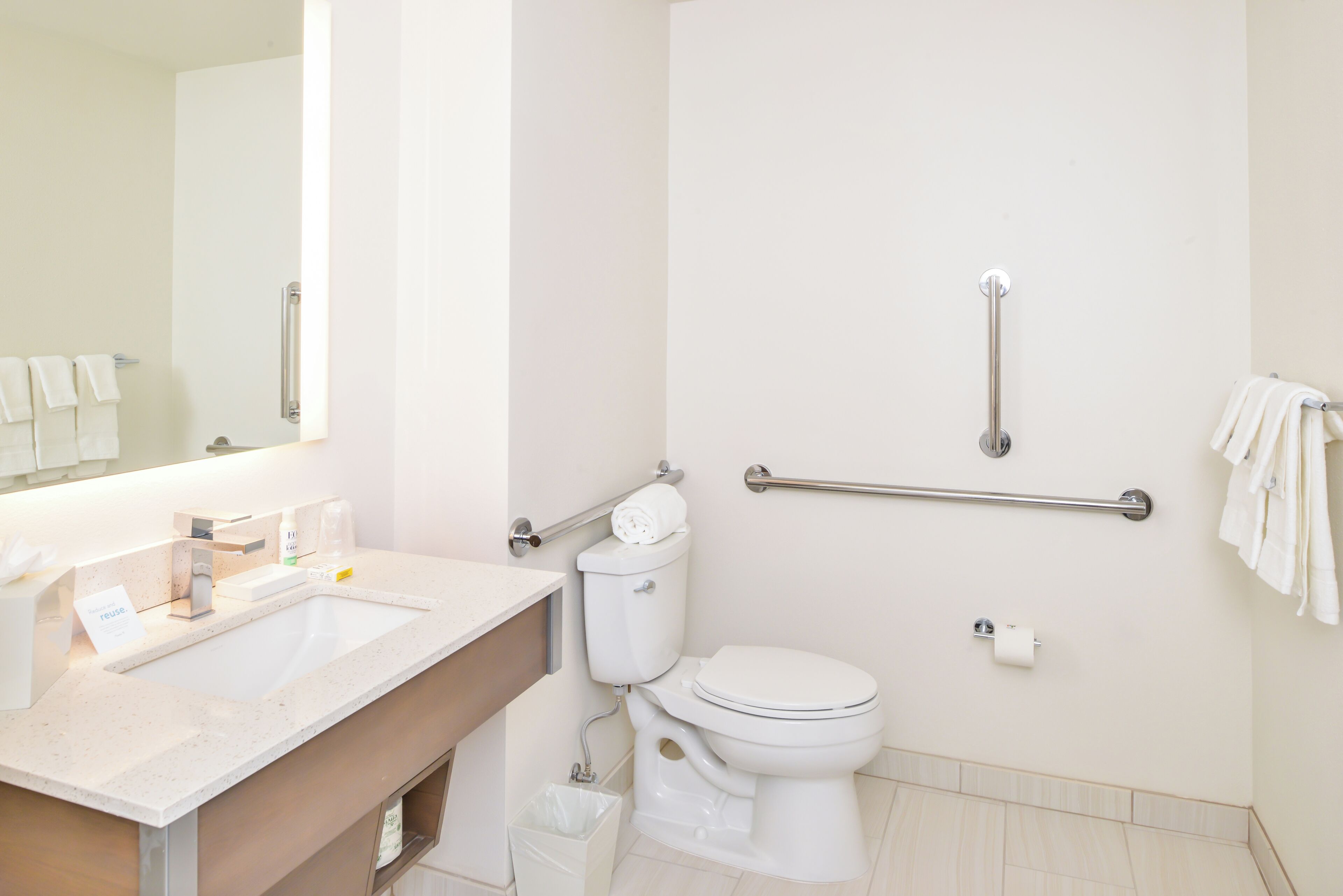 Un baño moderno con lavamanos, inodoro y barras de apoyo.