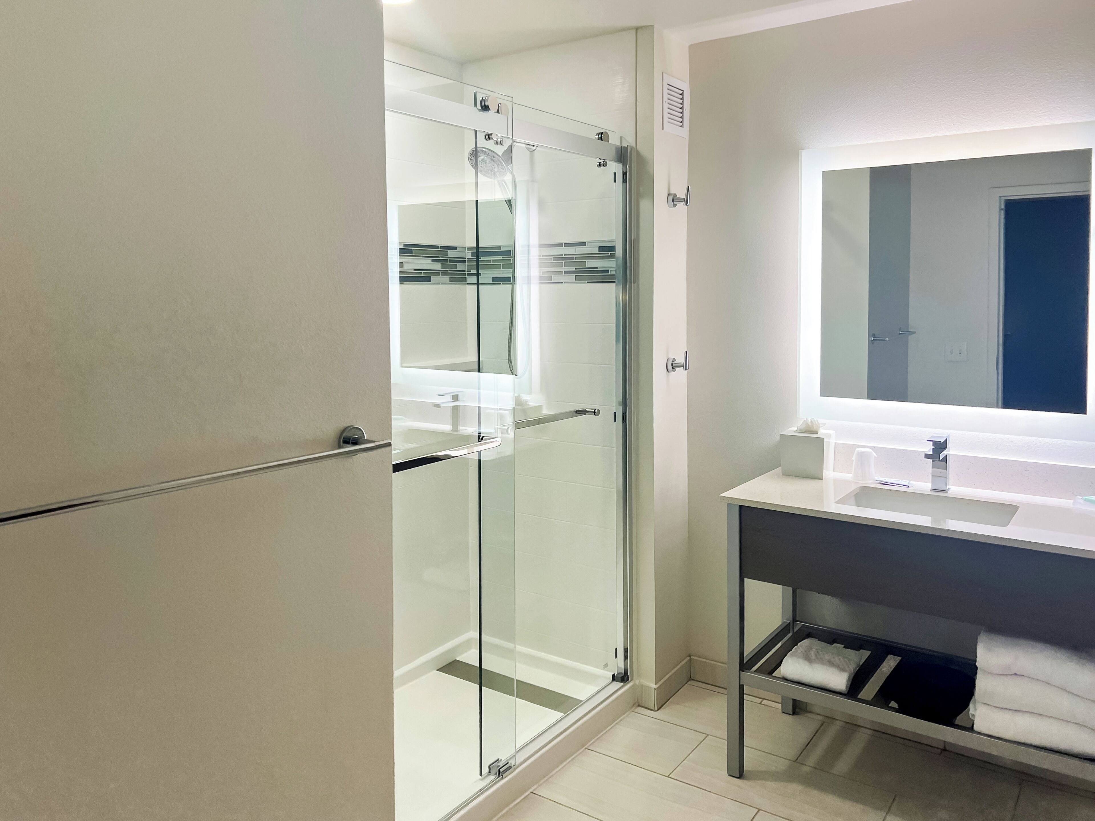 A modern bathroom with a glass shower enclosure, a white sink with a mirror above it, and a towel rack.