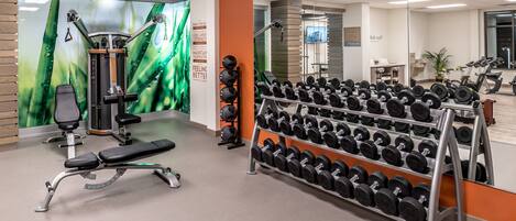 Un gimnasio con equipo de ejercicio, una banca y un estante con mancuernas.
