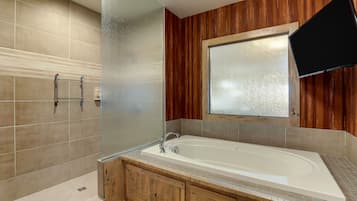A bathroom with a bathtub, wooden cabinetry, a glass shower enclosure, and a mounted television.