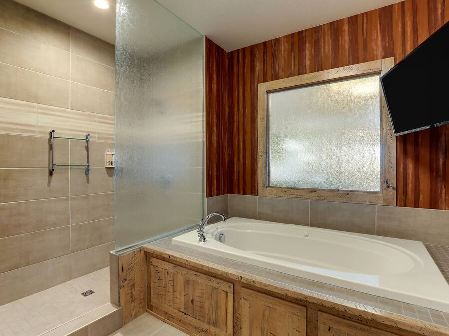 A bathroom with a bathtub, wooden cabinetry, a glass shower enclosure, and a mounted television.