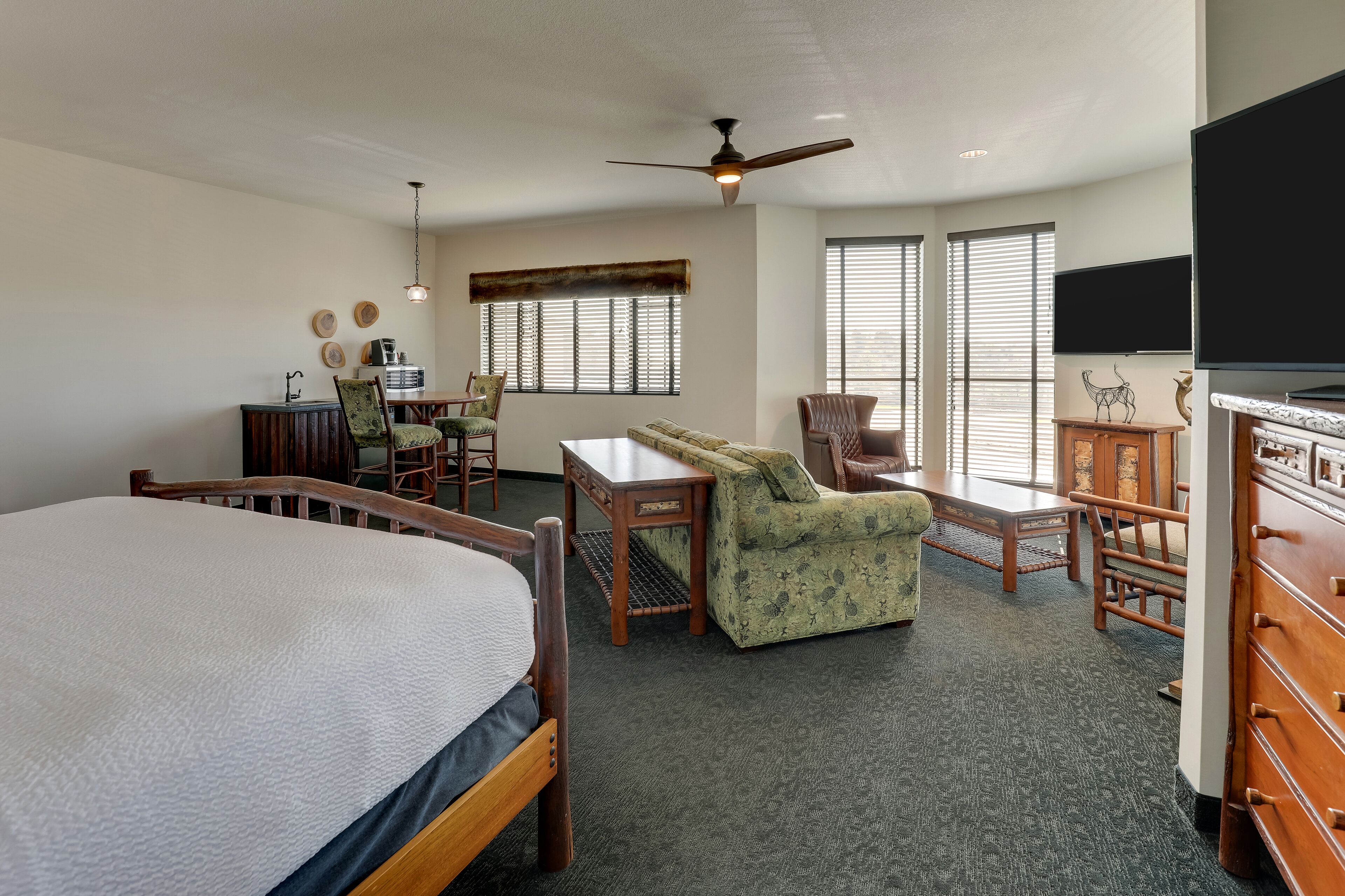 A hotel room with a large bed, a desk, two chairs, a sofa, a ceiling fan, and a television.
