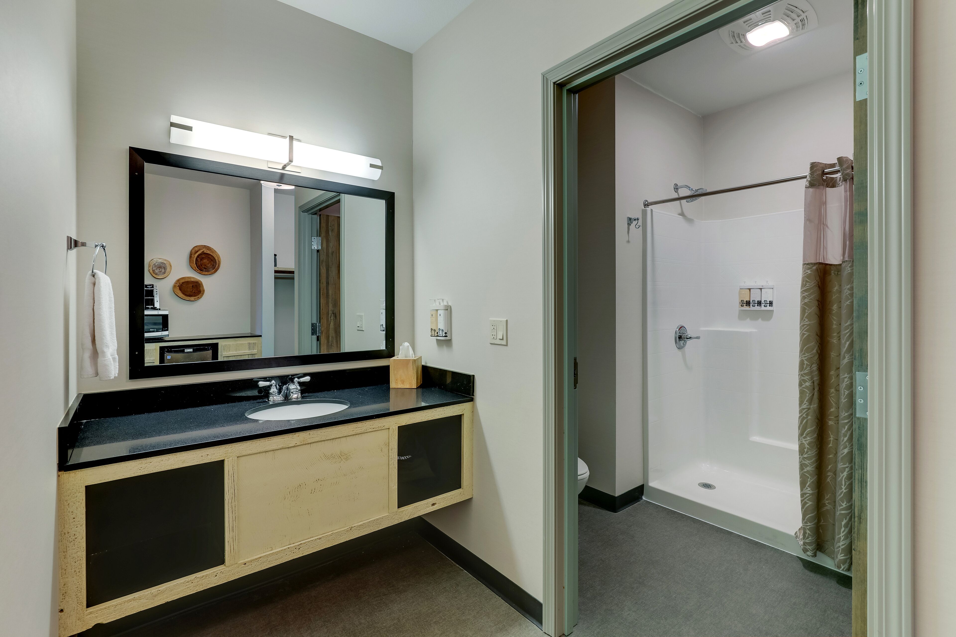 Een moderne badkamer met een zwart aanrechtblad, een wastafel, een spiegel en een douche met glazen wanden.