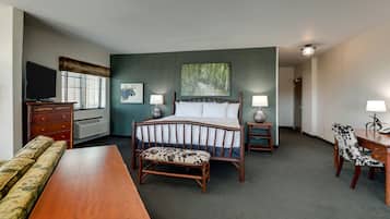 Habitación de hotel con cama, mesitas de noche, escritorio, silla, televisor y ventana con persianas.