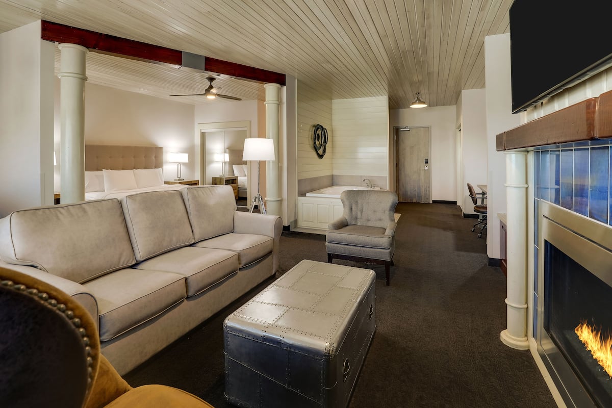 Un salón espacioso con chimenea, un sofá grande, un sillón más pequeño y una mesa de centro.