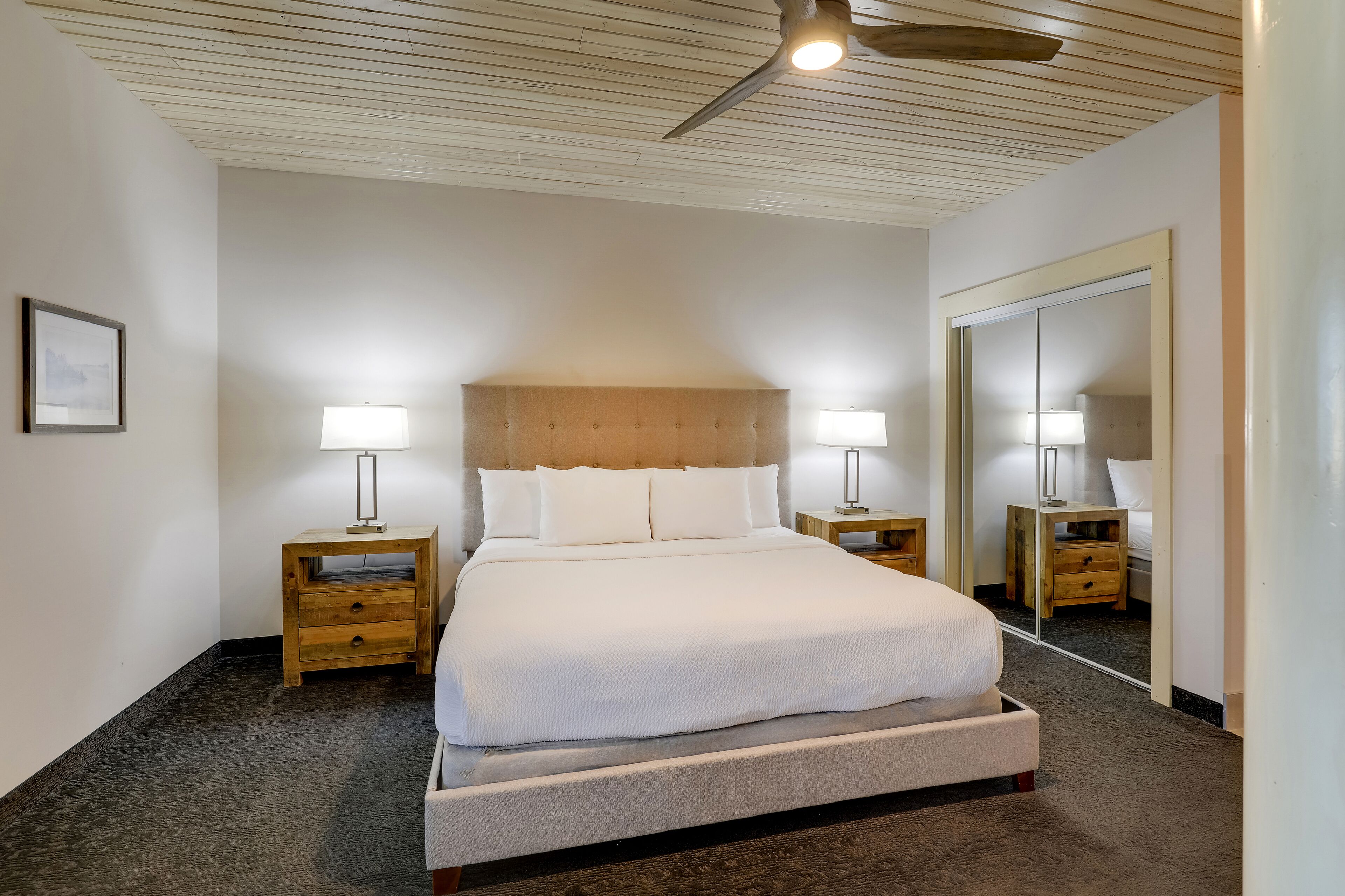 A neatly arranged hotel room with a large bed, two bedside tables with lamps, a ceiling fan, and a large mirror on the wall.