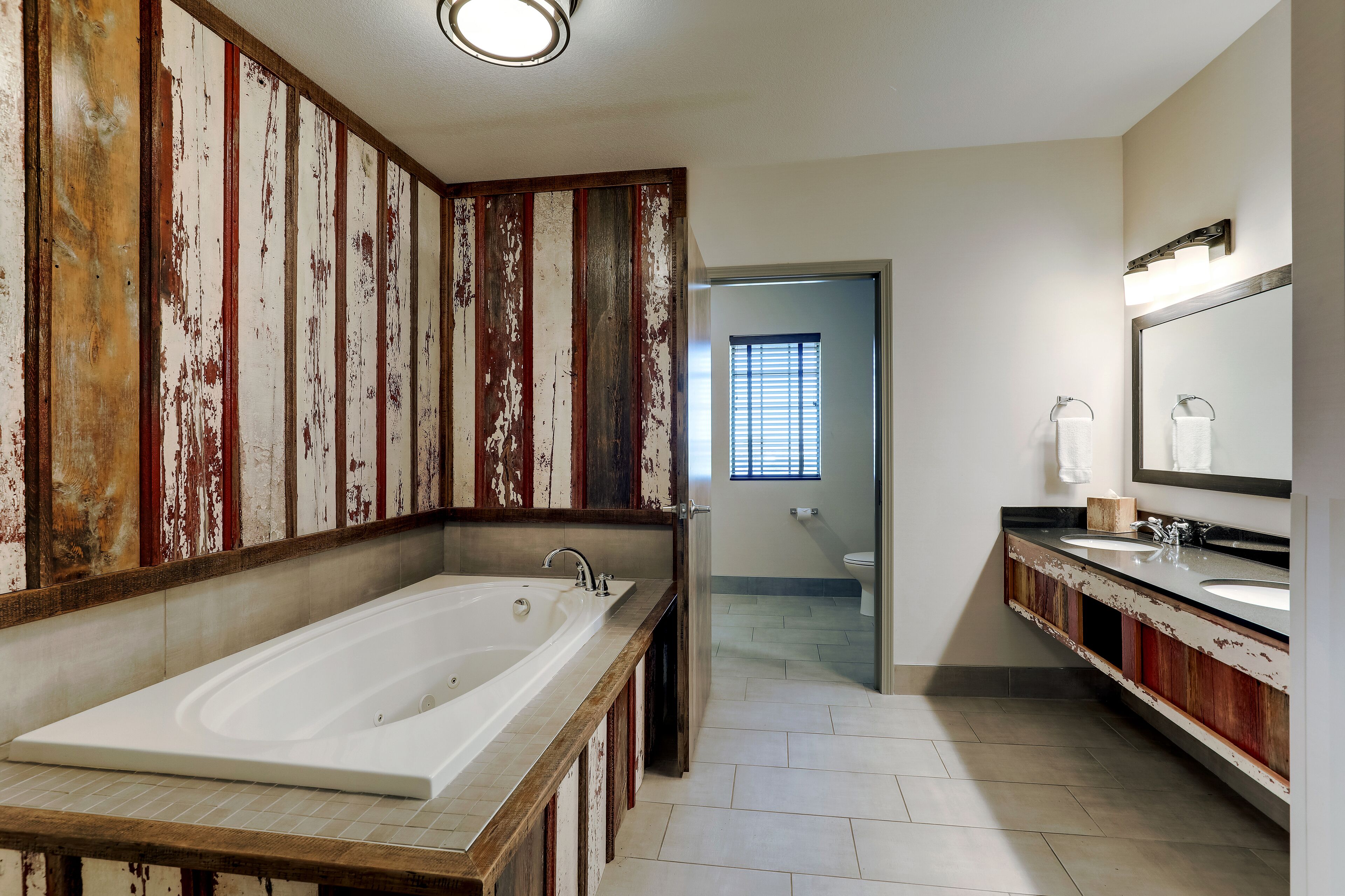 A bathroom with a large bathtub, a double sink vanity, and a mirror.