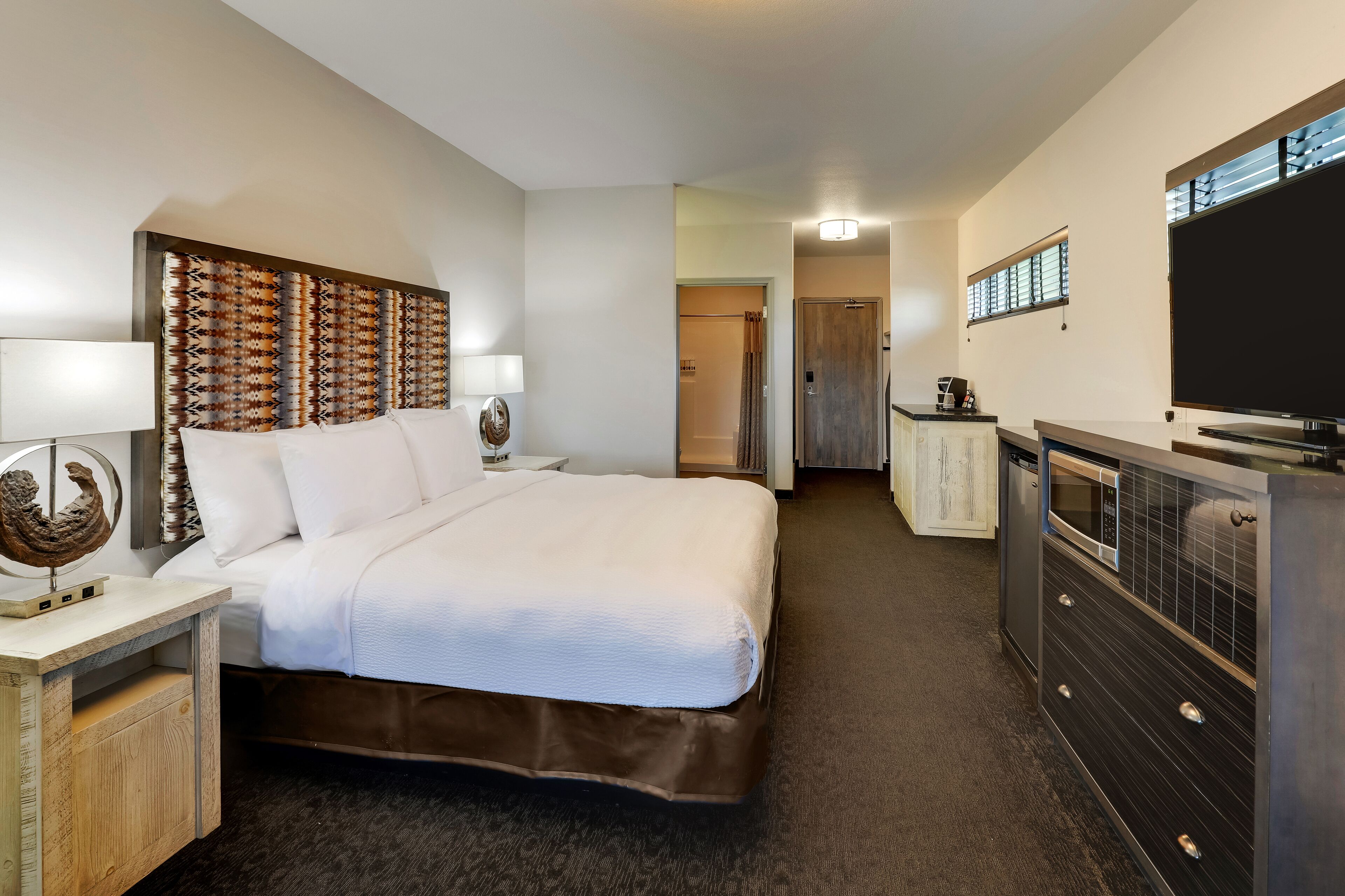 Una camera d'albergo con un letto grande, una cassettiera, una televisione e un bagno sullo sfondo.