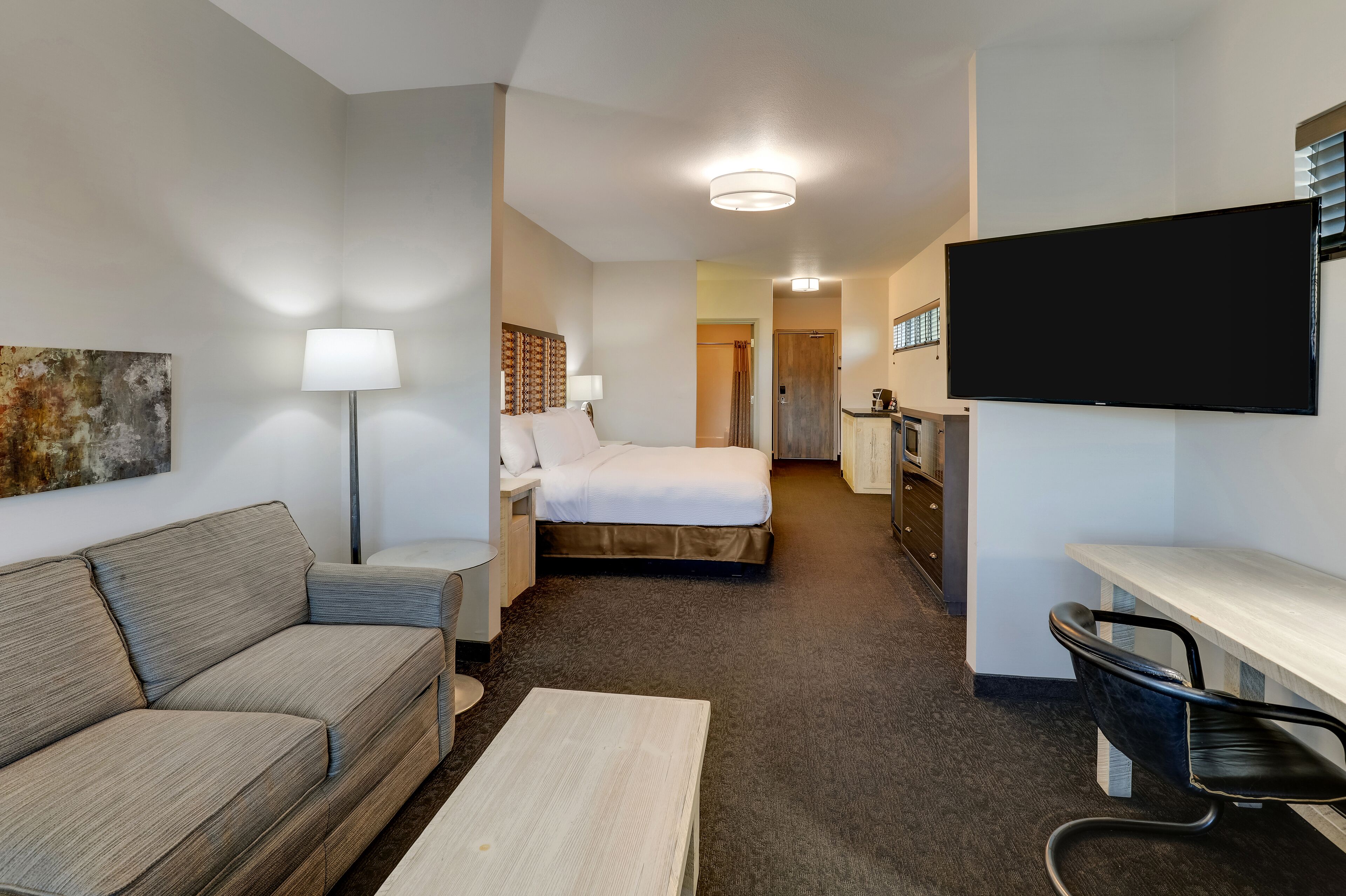A hotel room with a sofa, a bed, a desk, a TV, and a lamp.