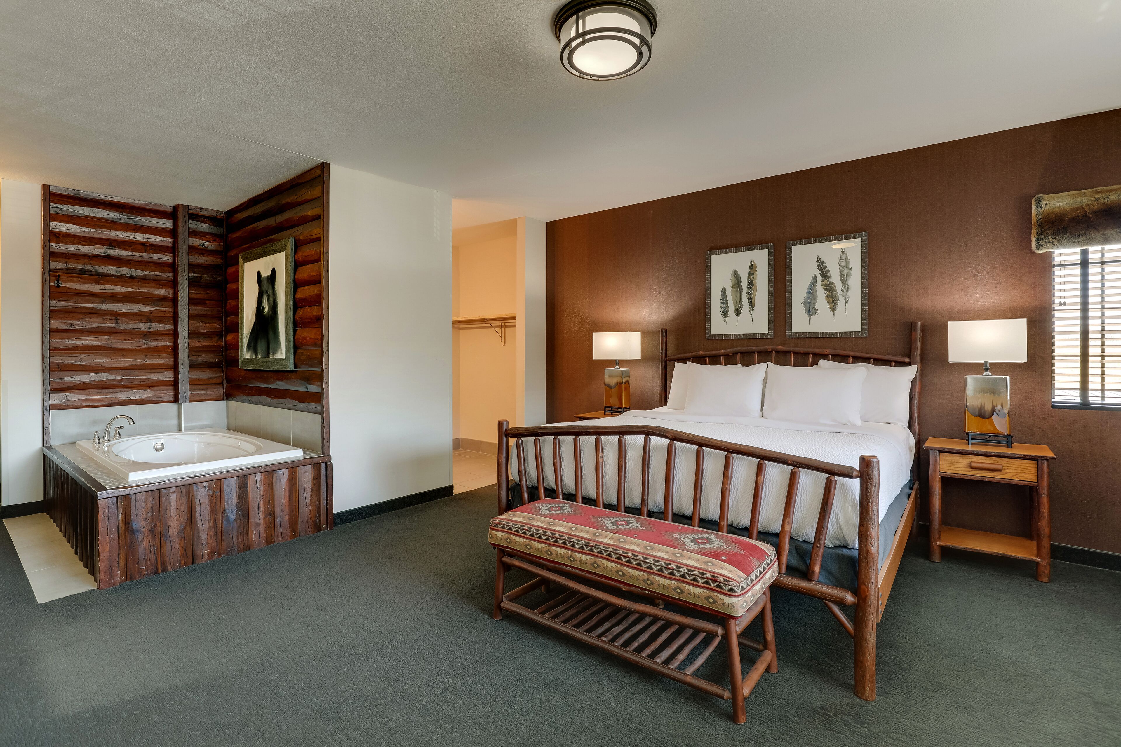 Ein Hotelzimmer mit Holzwand, einem großen Bett, einer Holzbank, einer Badewanne und zwei Wandleuchten.