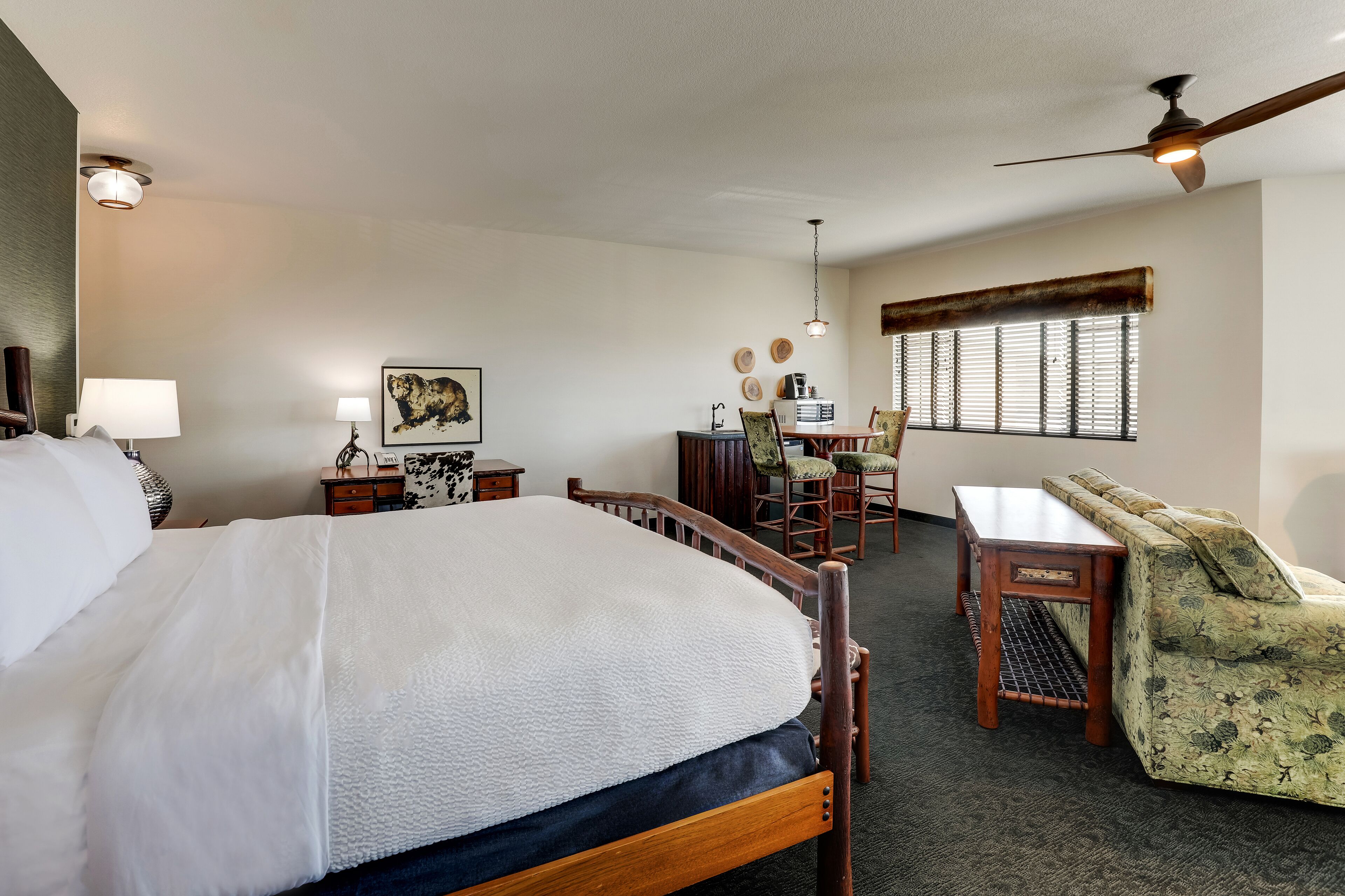 A hotel room with a large bed, a desk with a chair, a sofa, and a ceiling fan.