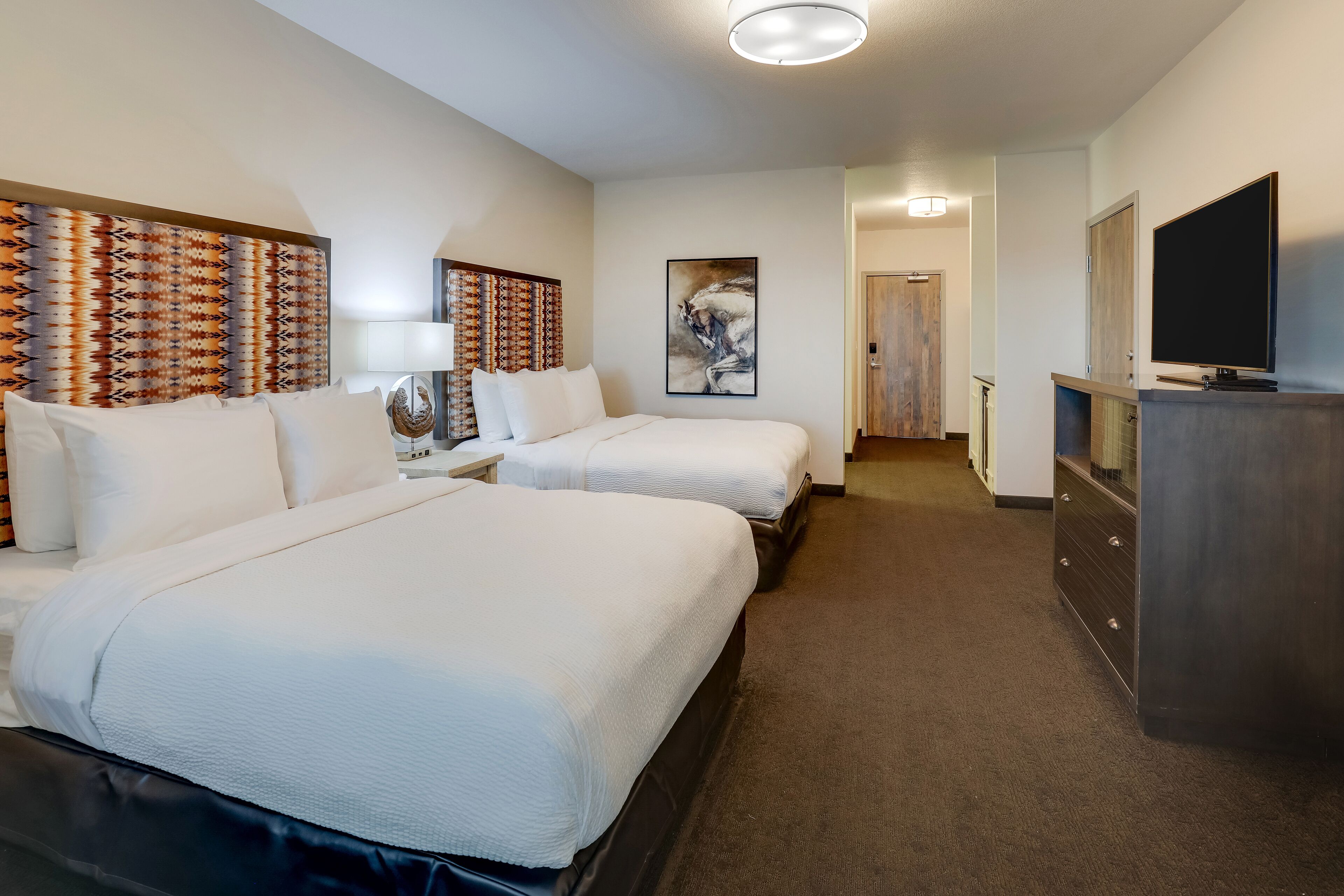 Une chambre d’hôtel avec deux lits, une télévision, une commode et un tableau au mur.