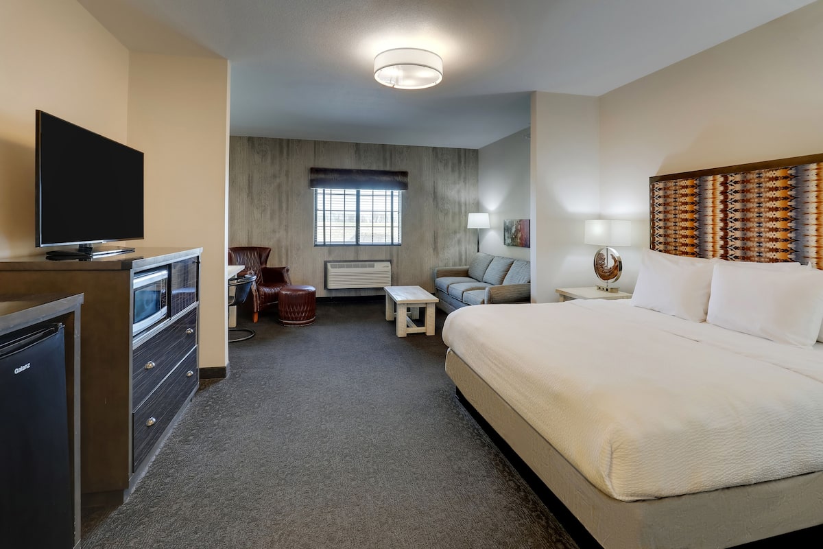 Habitación de hotel con cama, televisor, escritorio con computadora, silla, una mesita y una lámpara.