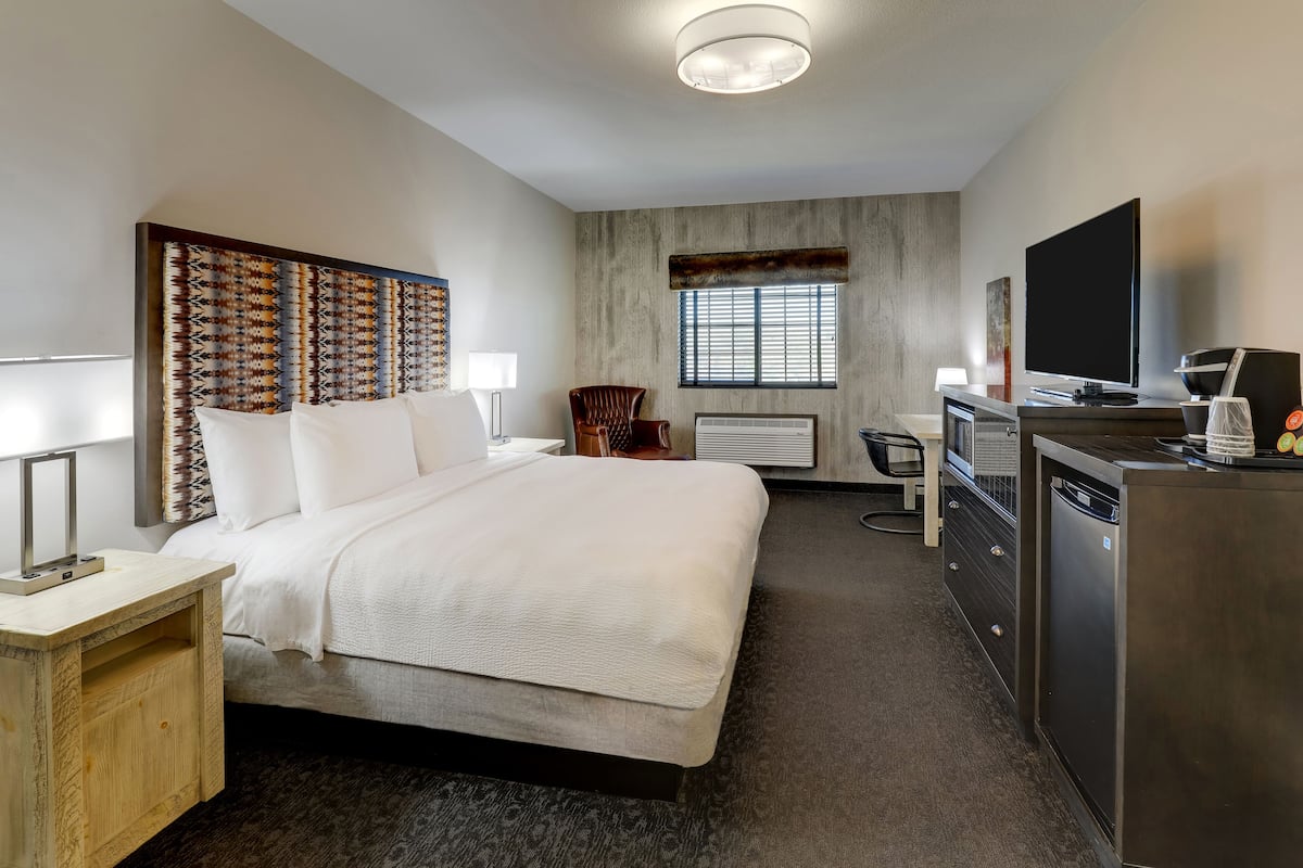 Habitación de hotel con cama, mesita de noche, lámpara, silla, escritorio, televisor y lavadora secadora integradas.