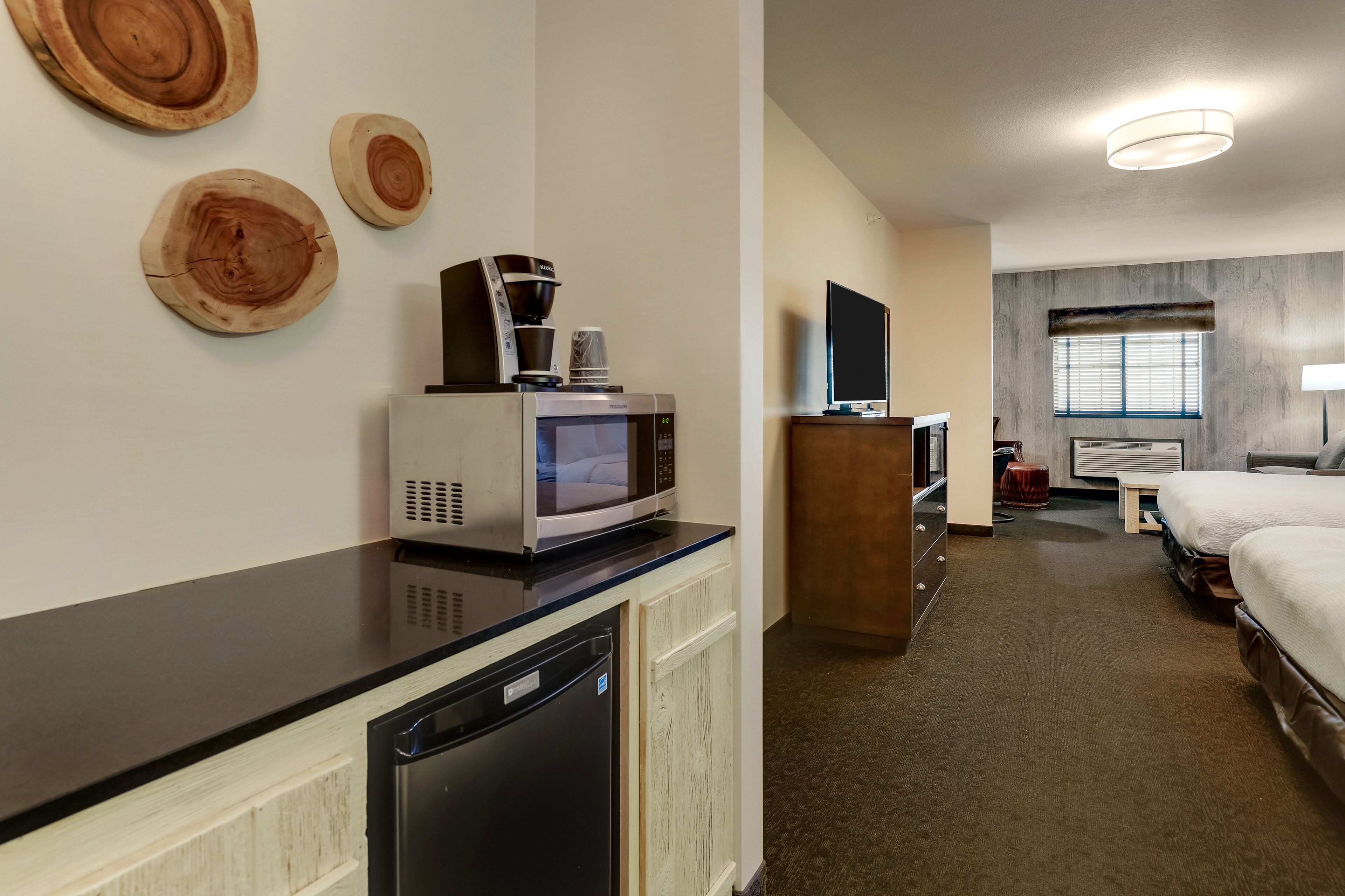 A hotel room with a kitchenette, a bed, a TV, and a window with blinds.